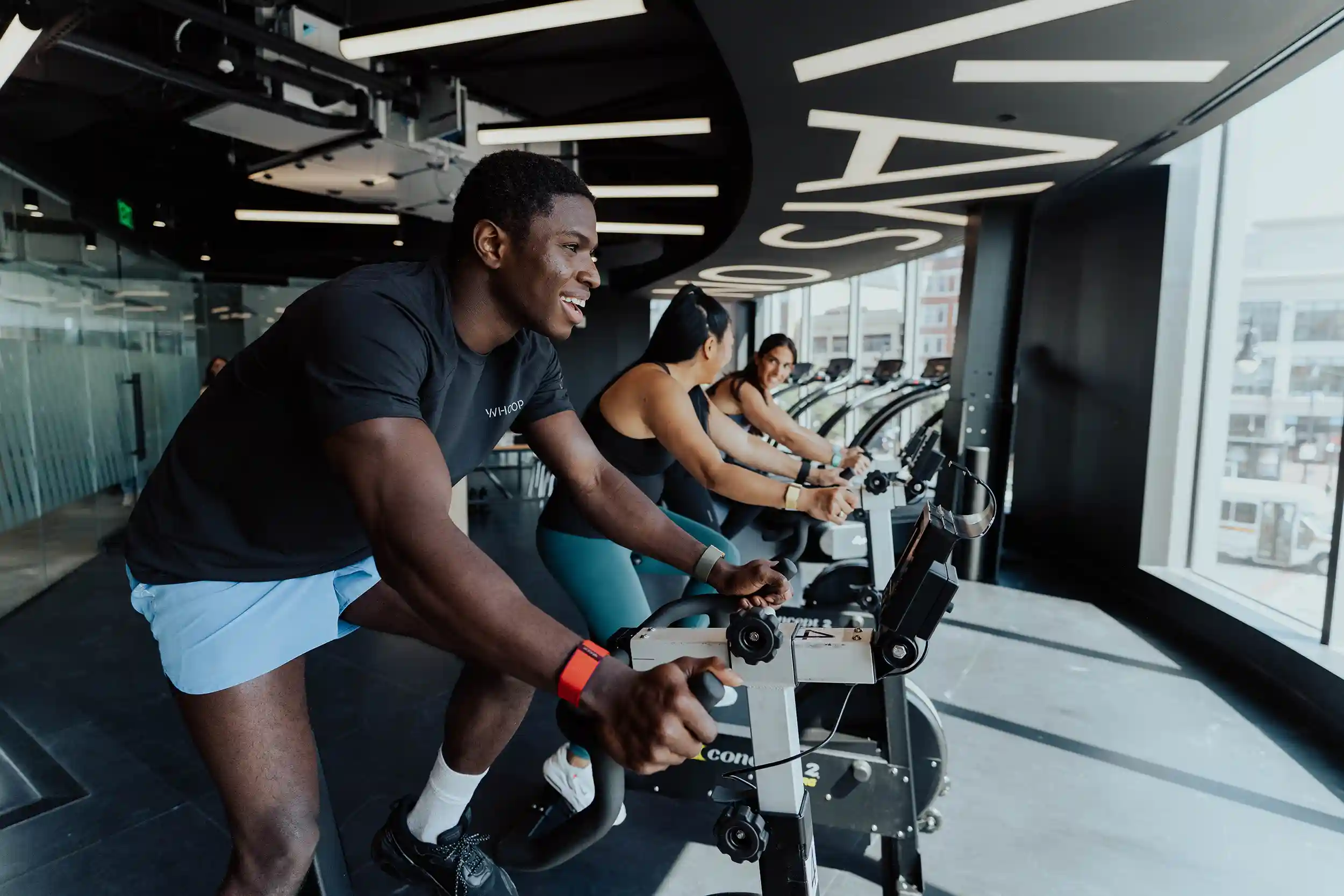 A man wearing a WHOOP 4.0 Band smiles while cycling on a stationary bike during a WHOOP Lab study.